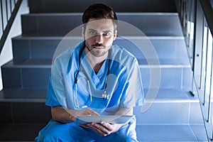 Portrait of male nurse sitting on staircase and using digital tablet