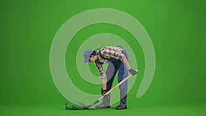 Portrait of male in overalls and rubber boots on chroma key green screen. Man gardener digging a hole in the soil with