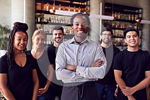 Portrait Of Male Owner Of Restaurant Bar With Team Of Waiting Staff Standing By Counter