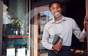 Portrait Of Male Owner Of Start Up Coffee Shop Or Restaurant Standing In Doorway With Digital Tablet