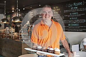 Portrait Of Male Owner With Tray Of Muffins In Coffee Shop