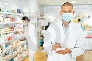 Portrait of male pharmacist in protective mask, working in pharmacy during the pandemic, standing in trading floor and