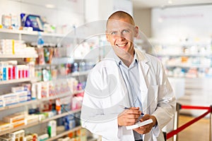 Portrait of male pharmacist working in pharmacy during the pandemic, standing in trading floor and makes important notes