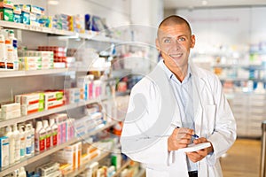 Portrait of male pharmacist working in pharmacy during the pandemic, standing in trading floor and makes important notes