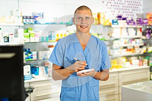 Portrait of male pharmacist working in pharmacy during the pandemic, standing in trading floor and makes important notes