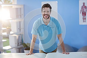 Portrait of male physiotherapist standing near massage bed