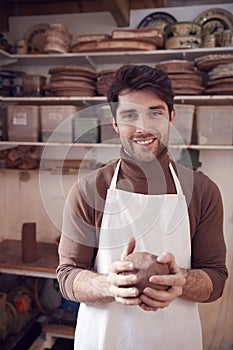 Portrait Of Male Potter Wearing Apron Holding Lump Of Clay In Ceramics Studio