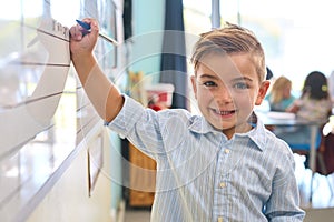 Portrait Of Male Primary Or Elementary School Student Writing On Whiteboard In Classroom Lesson