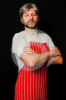 Portrait of a male professional butcher on a dark background. The model is in his 40s, grey hair and beard, dressed in red and