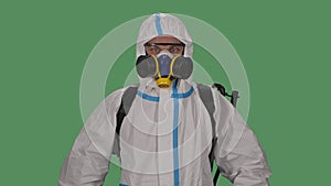 Portrait male in a protective suit, safety glasses, gloves and a respirator looks confidently into the camera and then