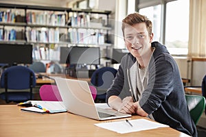 Portrait Of Male Student Working At Laptop In College Library