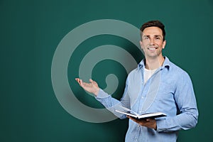Portrait of male teacher with book on color background