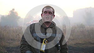 Portrait of male tired firefighter in uniform at smoky lawn after fire. Young fireman standing at countryside against