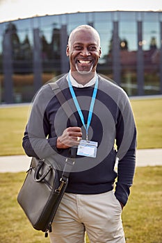 Portrait Of Male University Or College Tutor Outdoors With Modern Campus Building In Background