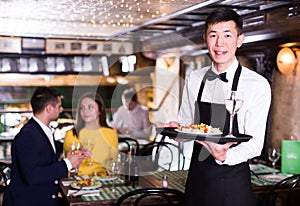 Portrait of male waiter who is holding tray with order