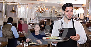Portrait of male waiter who is holding tray with order