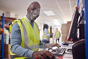 Portrait Of Male Worker In Busy Modern Warehouse Working On Computer Terminal