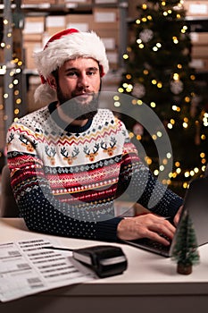 Portrait of male worker in busy modern warehouse working on laptop computer, Christmas sale concept