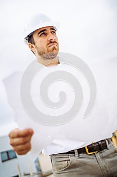 portrait of male worker on construction site, wearing hard hat and reading blueprints