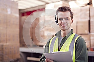 Portrait Of Male Worker At Freight Haulage Business Standing By Truck Being Loaded By Fork Lift 