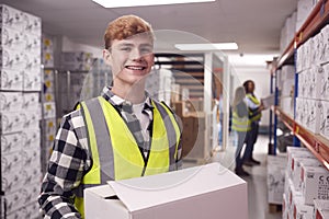 Portrait Of Male Worker Inside Busy Warehouse Carrying Box