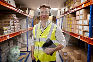 Portrait Of Male Worker Wearing Headset In Logistics Distribution Warehouse Using Digital Tablet