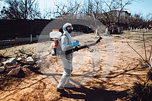 Portrait of male worker wearing protective clothing and spraying insecticide in fruit orchard