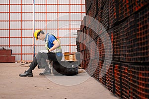 Portrait of a male worker wearing a safety vest and helmet sitting on a steels pallet due to back pain