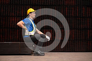 Portrait of a male worker wearing a safety vest and helmet sitting on a steels pallet due to back pain