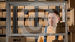 Portrait of male working in storage. Man storekeeper with frustrated face throws box on the shelf other packages falling