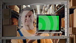 Portrait of male working in storage. Man storekeeper standing near rack with boxes holding laptop with chroma key green