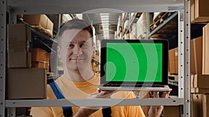 Portrait of male working in storage. Man storekeeper standing near rack with boxes holding laptop with chroma key green