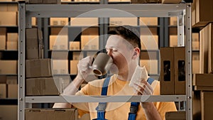 Portrait of male working in storage. Man storekeeper standing near rack eating sandwich drinking coffee from a mug