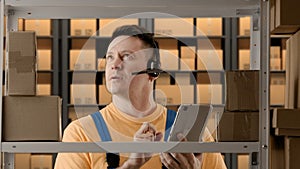 Portrait of male working in storage. Man storekeeper standing near rack in headset talking and checking goods