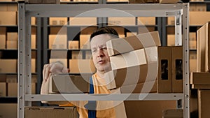 Portrait of male working in storage. Man storekeeper standing near rack taking boxes holding big stack in hands and