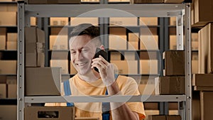 Portrait of male working in storage. Man storekeeper standing near rack talking on smartphone about orders, smiling