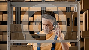 Portrait of male working in storage. Man storekeeper standing near rack talking on smartphone about orders, smiling