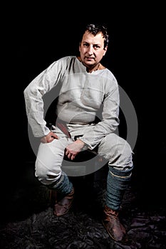 Portrait of a man in an ancient shirt and trousers from unbleached linen. A man sits and looks directly at the camera.