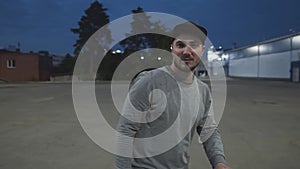 Portrait of a Man in a Baseball Cap Among the Night City Lit by Lanterns. Floored Camera Movement. A Man at Night Looks