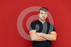 Portrait of a man with a beard and a blue t-shirt on a red background, looks into the camera with a serious face. Bearded man