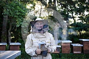 Portrait of man beekeeper working in apiary, holding bee smoker.