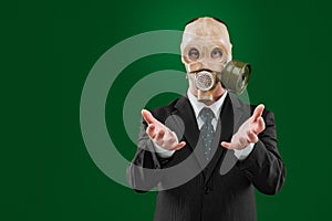 Portrait of a man begging, wearing a dark business suit and a gas mask, isolated on green background