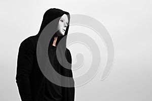 Portrait of man in black hoodie wearing white anonymous mask.