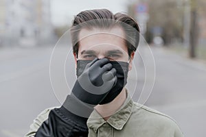 Portrait of a man in a black medical mask.. The man adjusts his mask with a black gloved hand