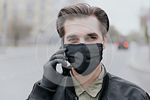 Portrait of a man in a black medical mask.. A man is talking on the phone