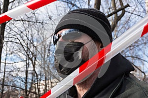 Portrait of a man in a black protective mask against a background of tree branches and a blue sky.The concept of social distance