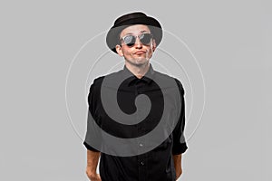 Portrait of a man in a black shirt, pork pie and sun glasses hat isolated over grey background.