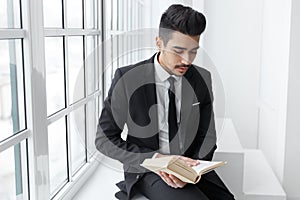 Portrait of an man in black suit drinking coffee and looking at open book