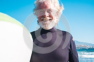 Portrait of man with a black wetsuit holding a surftable ready to go surf at the beach with the sea or ocean in the background -