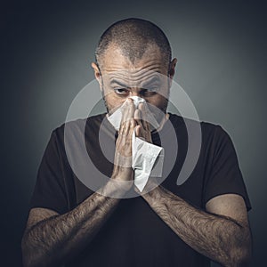 Portrait of a man blowing his nose with a tissue. look at the camera